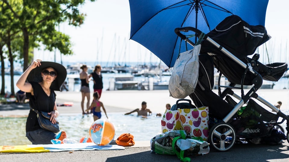 ina dunna cun chapè sper il Lac Léman, dasperas ina carrotscha d'uffants sut in parasol
