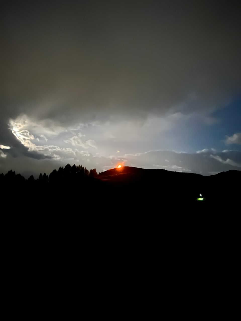 Der Himmel ist in der Nacht klar, jedoch auch mit Nebel bedeckt. Man sieht das Höhenfeuer aus der Ferne.