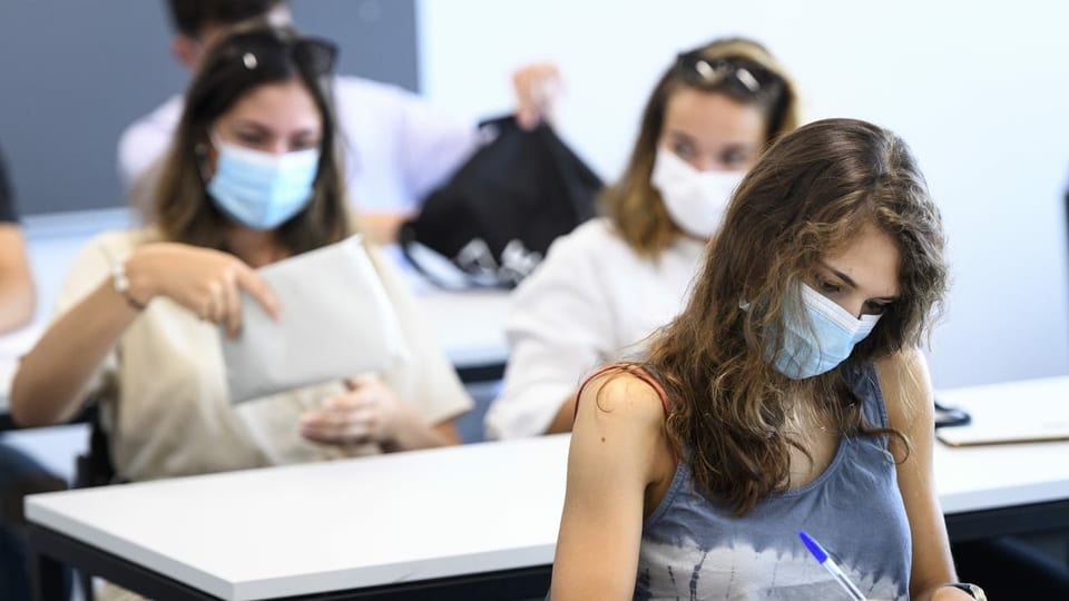 Purtret da scolaras ad in gimnasi che portan mascras da protecziun durant l'instrucziun. 