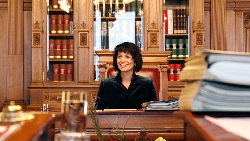 Doris Leuthard, en in biro vegl cun plunas d'actas dasperas.