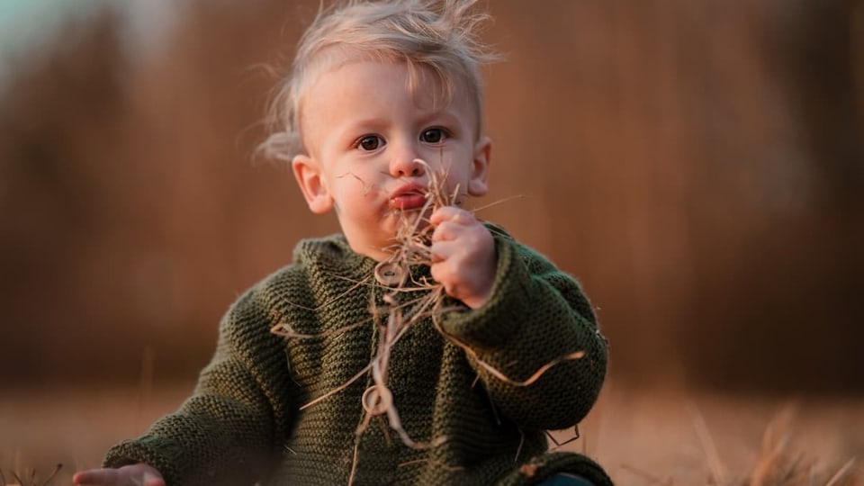 Kleinkind mit einer grünen Jacke sitzt auf einer Wiese | Rätoromanische Kindernamen