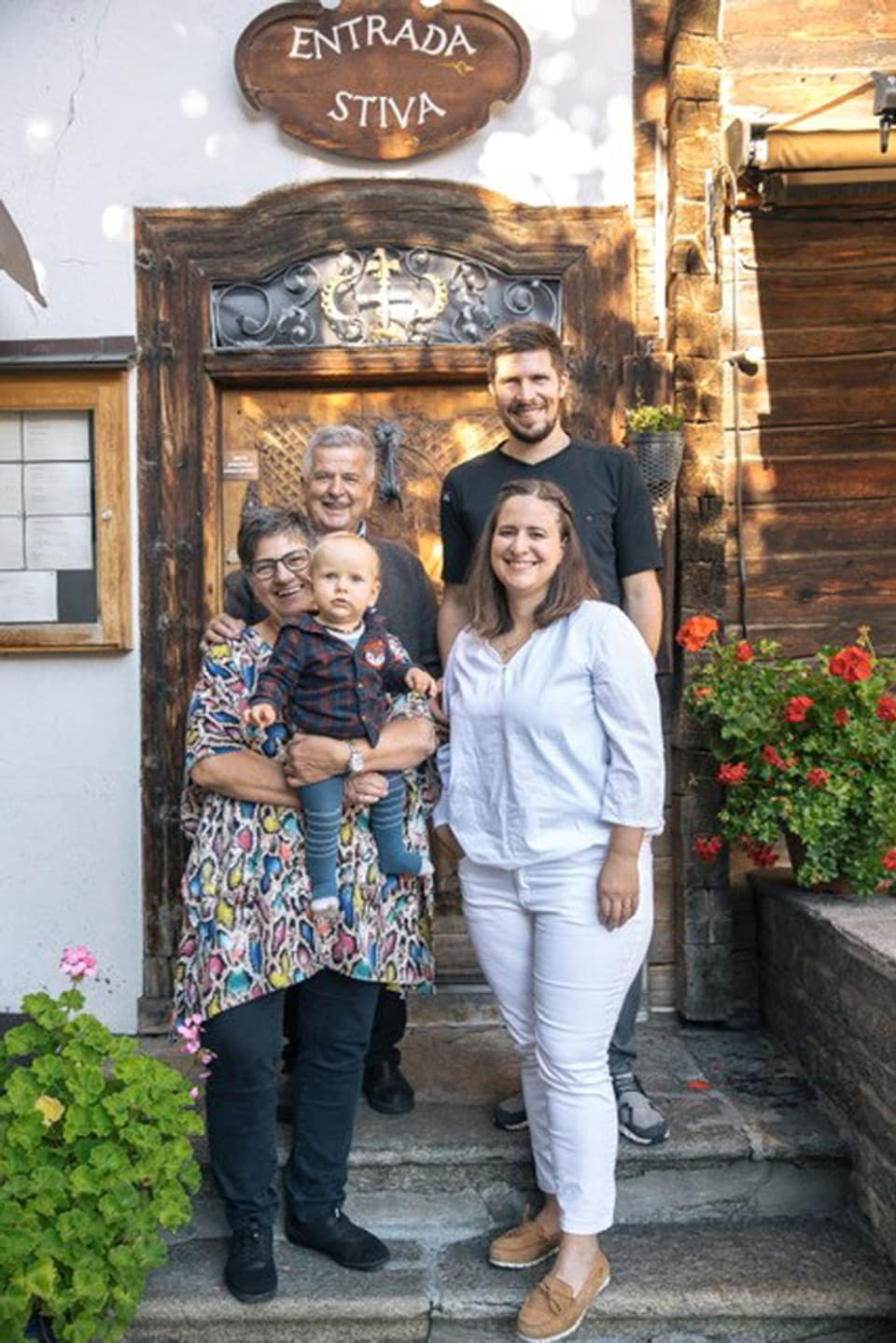 famiglia cun tat e tatta, geniturs e pop avant entrada d'ina chasa