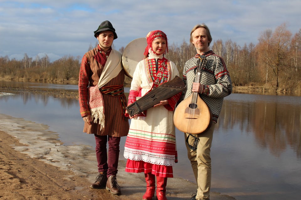 zwei Frauen und ein Mann in estnischer Tracht stehen an einem Fluss