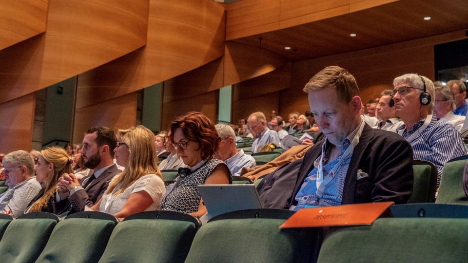 Persunas che sesan en ina sala da congress.