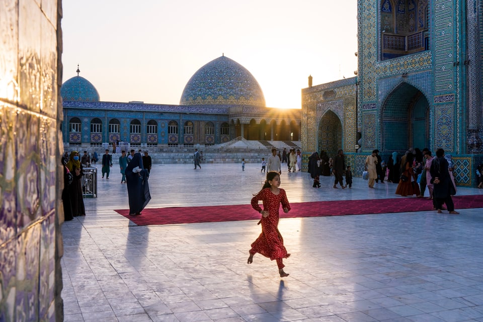 Ina buoba curra sur ina plazza gronda vi, davosvart in clutger d'ina moschea ed il sulegl che va da rendì. 