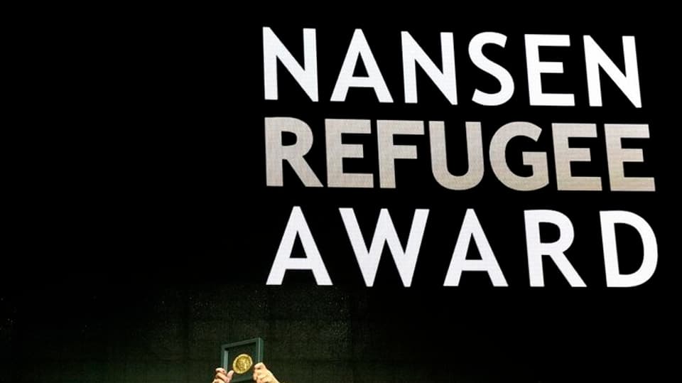 Projecziun dal scrit "Nansen Refugee Award" - fitg pitschen suten dus mauns che tegnan adaut ina medaglia enramada.