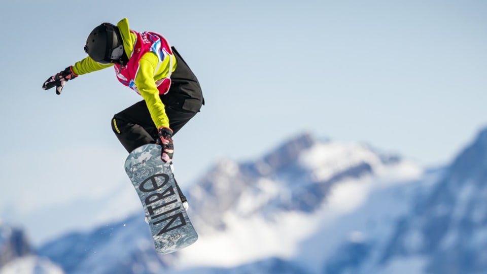 Ina snowboardista en l'aria davant ina culissa da culms.