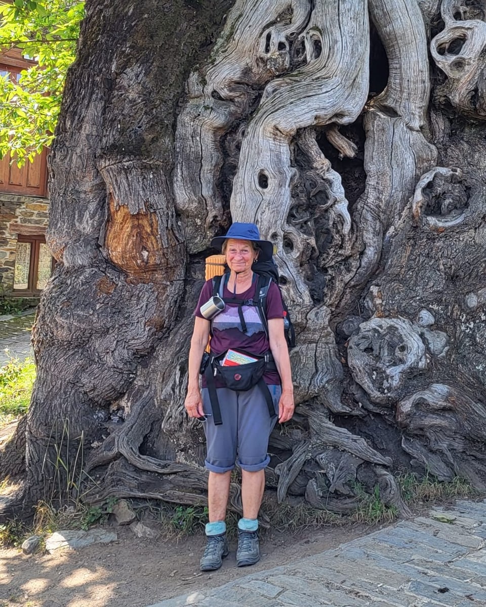 Judith Cantieni in ihrer Reisekleidung vor einem Baumstamm.