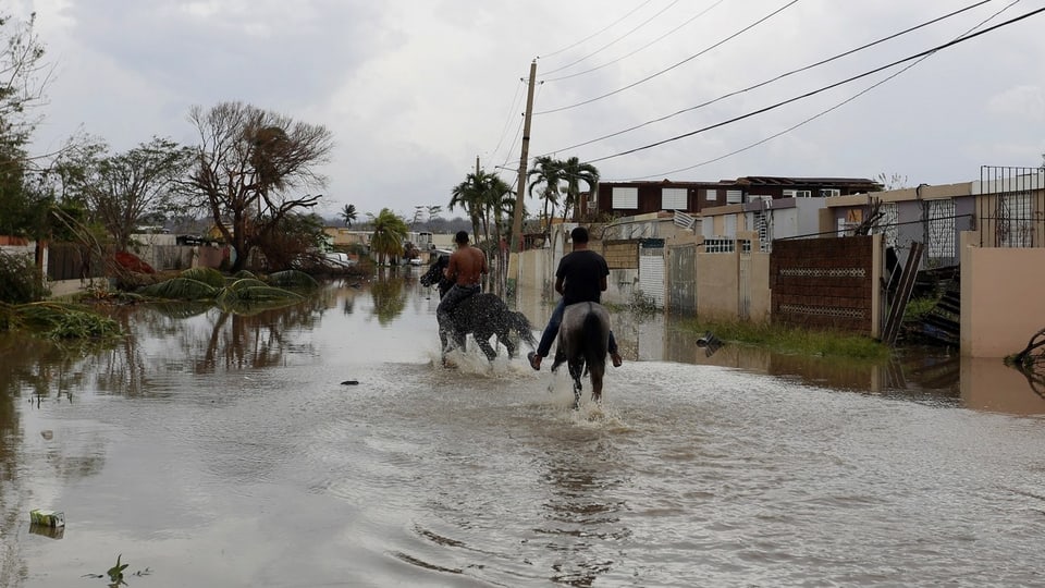 In lieu inundà cun chasas e duas persunas che traversan l'aua sin chavals.
