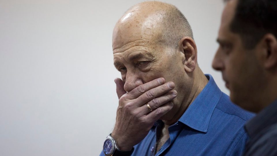 Ehud Olmert sa mussa schoccà e tegna ses maun dretg avant la bucca.