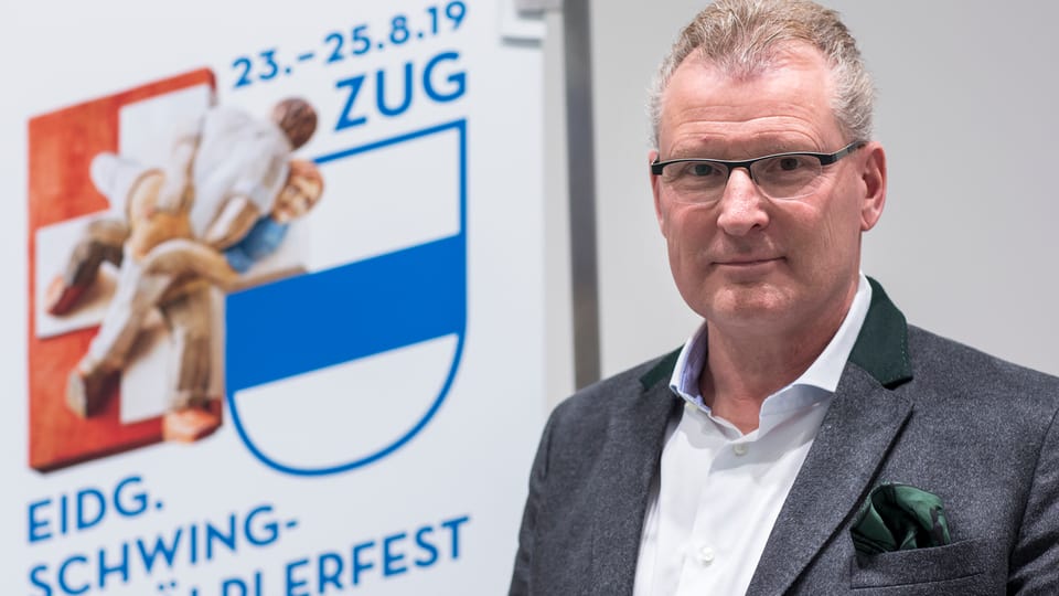 Purtret da Heinz Tännler davant il placat cun si la data da la festa. 