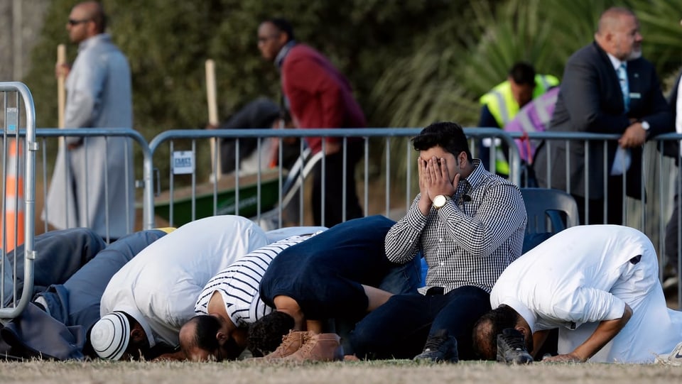 Purtret da muslims che fan oraziun giun plaun avant ina da las duas moscheas pertutgadas. 