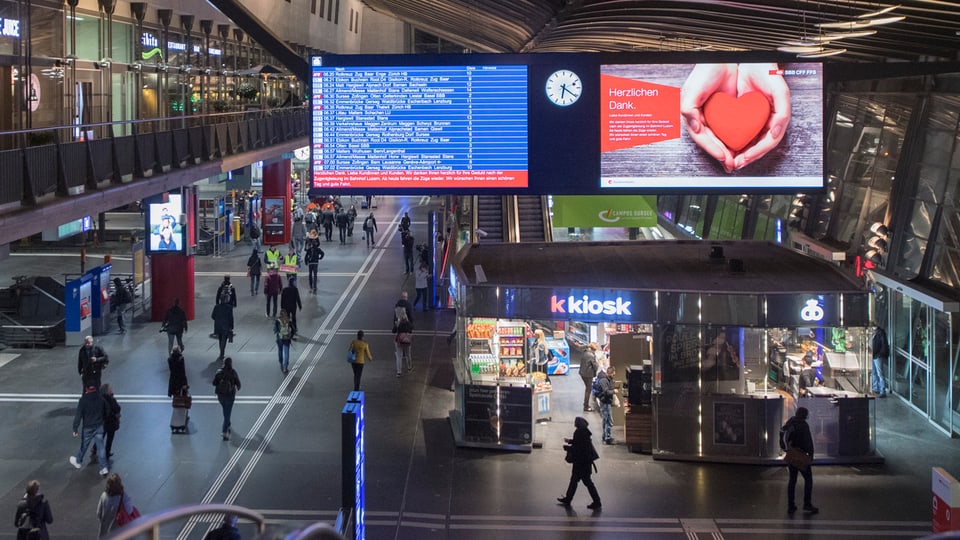 Staziun da tren cun in kiosc e passagiers sin ils perruns.