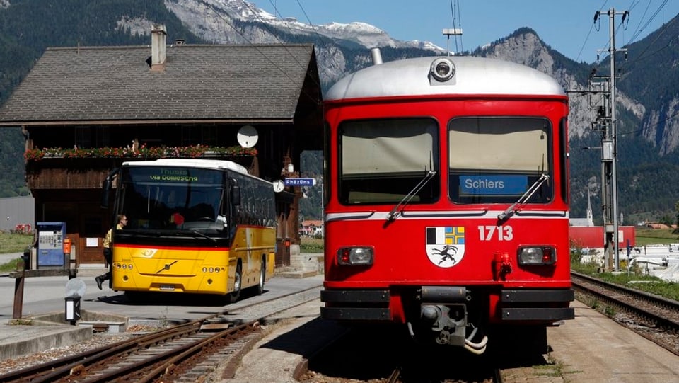in auto da posta ed in tren da la viafier retica a la staziun da Razén.