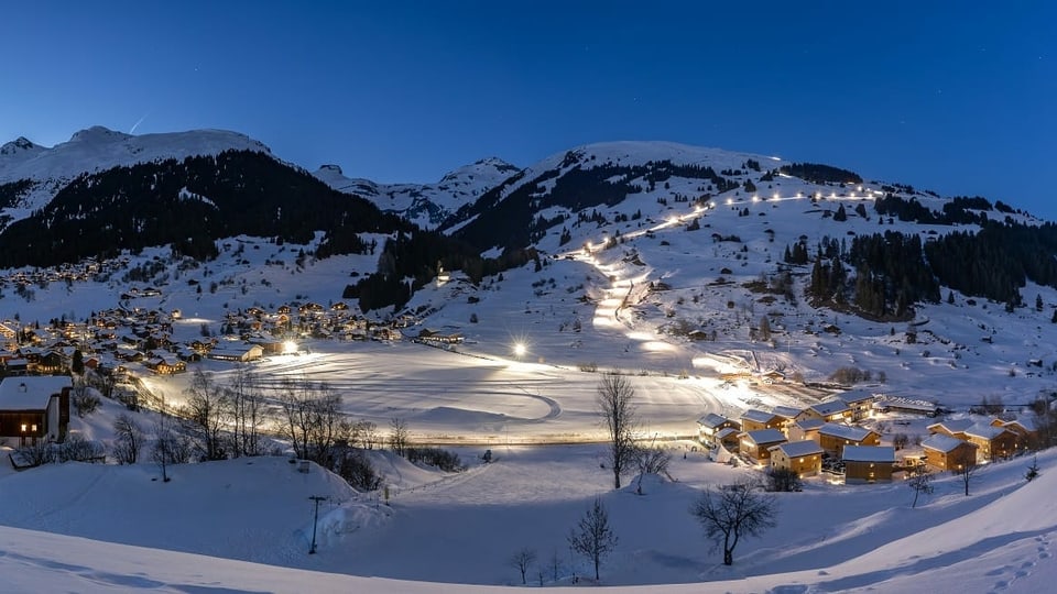 Il resort da vacanzas Pradas dretg e davos l'illuminada pista da skis. 