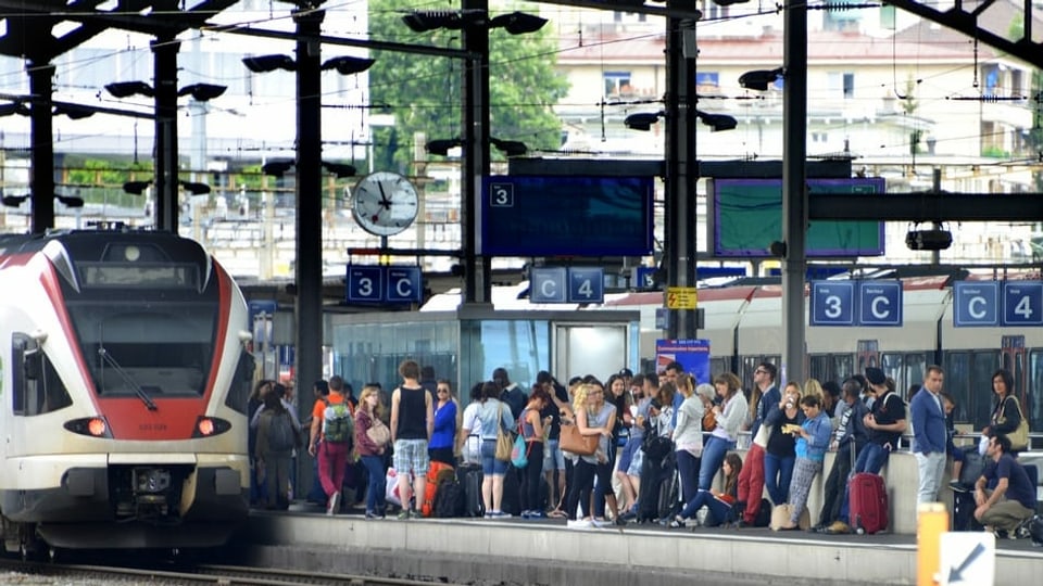 Staziun cun tren che arriva e blera glieud che spetga.