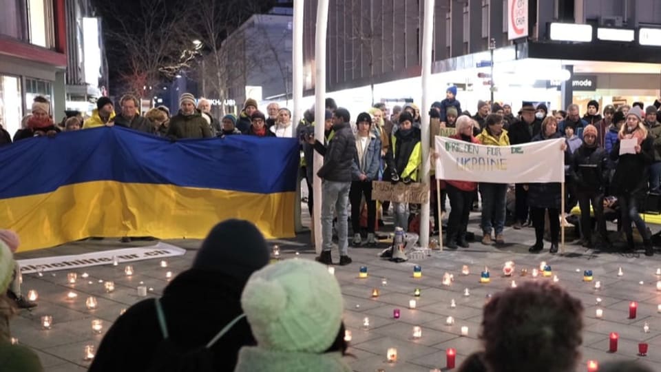 persunas che stattan en rudi enturn chandailas. entgins tegnan ina bandiera da l'Ucraina