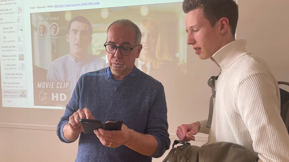 Lehrer und Schüler schauen in ein Handy.