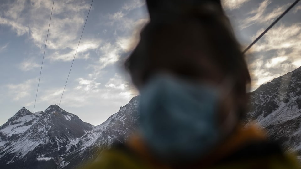 purtret d'ina persuna che porta ina mascrina davant ina culissa da muntogna. 