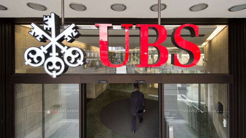Il logo da l'UBS avant ina porta d'ina filiala da banca. 