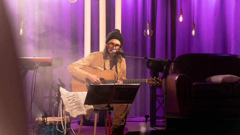 Künstler tumasch è auf der Bühne. Er spielt Gitarre.
