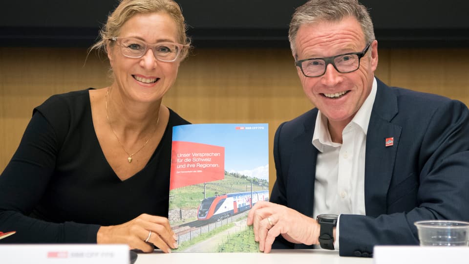 Els dus tegnan ina broschura cun si in tren.