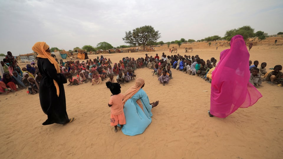 Ina scolasta ed uffants cuntinueschan cun l'instrucziun da scola. Els èn fugids da la guerra en il Sudan. 