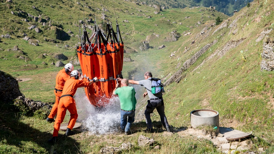 in transport d'au arriva, plirs umens svidan il satg che penda giu d'in helicopter.
